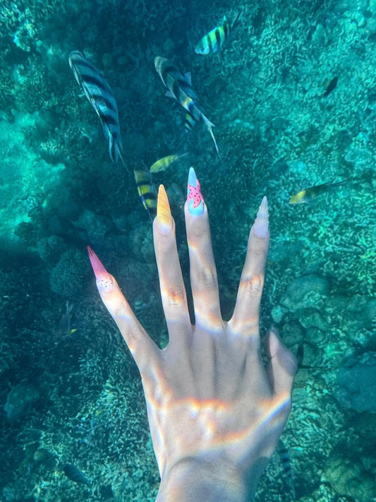 Hand with colorful Tsuki Nails press on nails underwater near tropical fish and coral reef