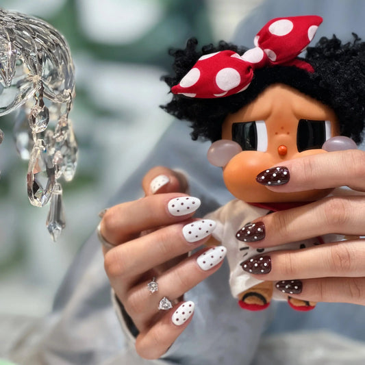Hands with Tsuki Nails press on nails in brown and white polka dot design, holding a doll