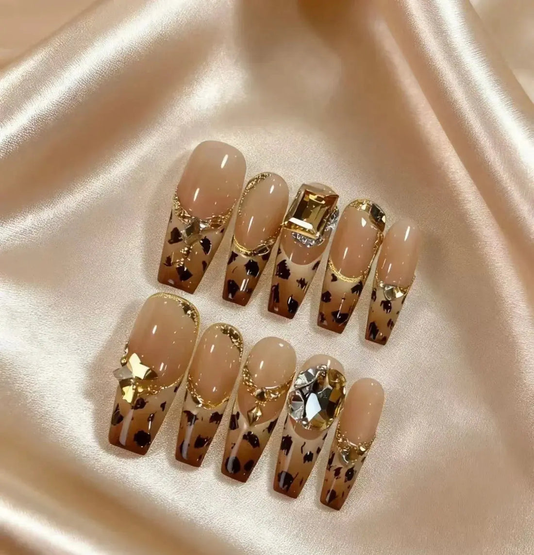 Leopard print press on nails with gold rhinestone accents on a satin surface, Tsuki Nails.