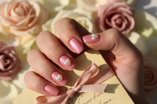 Baby pink chrome press on nails with 3D pearl heart accents, holding a vintage letter, roses in background
