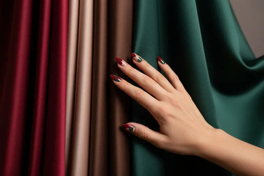 Hand with stylish press on nails touching red, nude, brown, green silk fabric for Tsuki Nails