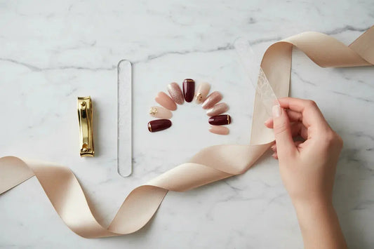 Luxury press on nails set, gold nail clipper, glass file, and silk ribbon on marble surface