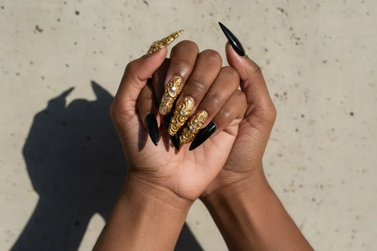 Two hands with Tsuki Nails press on nails, showcasing gold 3D art and glossy black stiletto tips