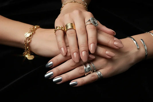 Hands with salon-quality nude and chrome press on nails, gold and silver jewelry on black cloth