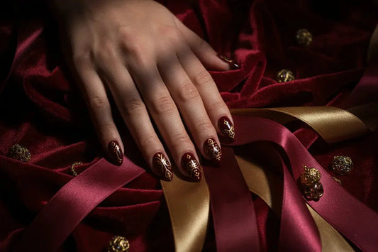 Close-up of a hand with deep crimson and gold press on nails on red satin, Tsuki Nails.
