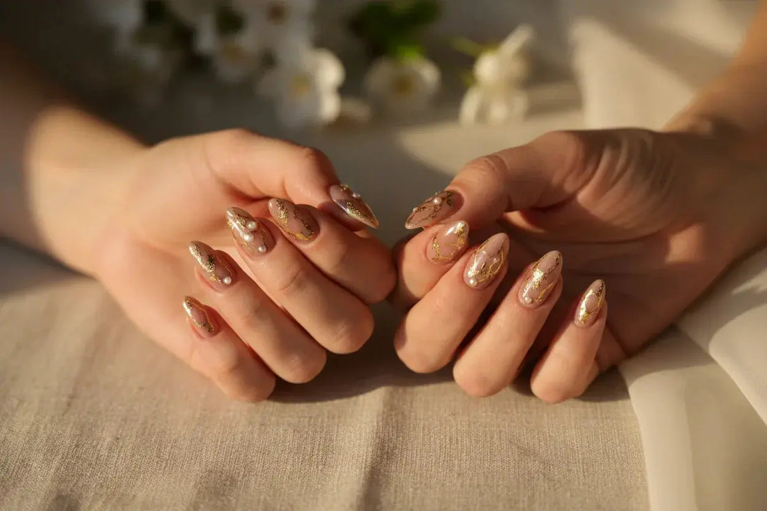 Two hands with matching Tsuki Nails press on nails, gold and pearl accents, in soft golden light