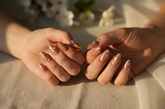Two hands with matching Tsuki Nails press on nails, gold and pearl accents, in soft golden light