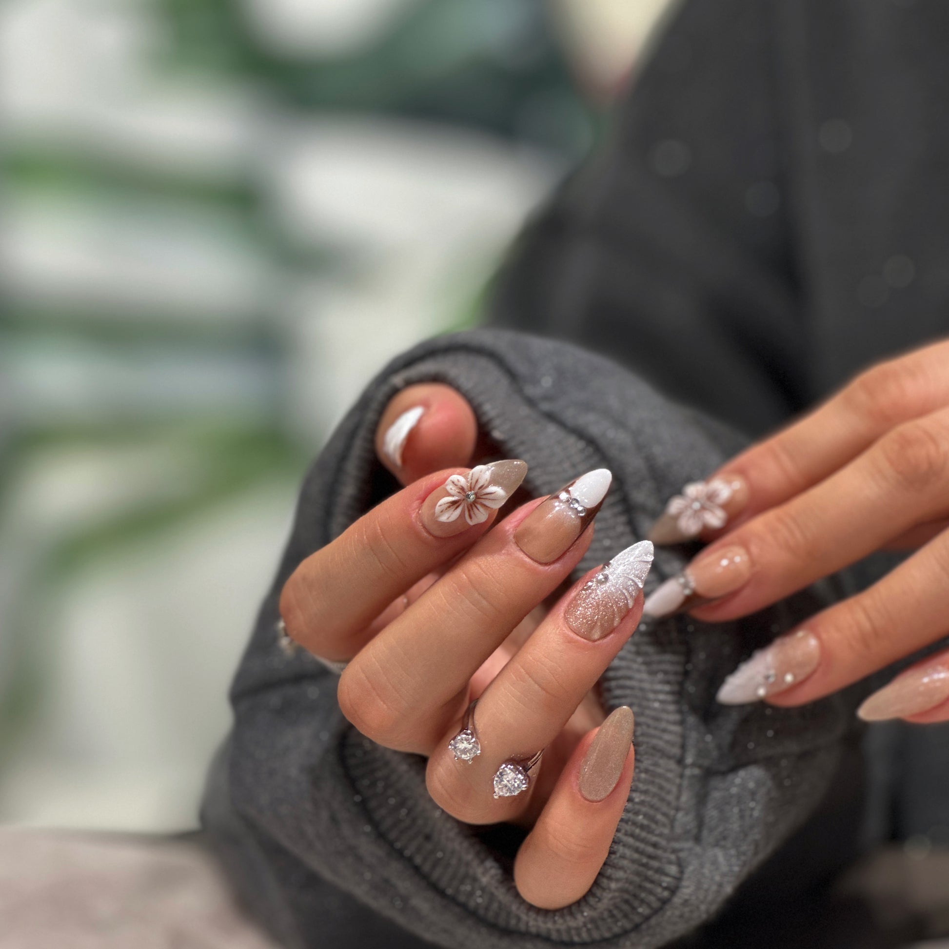 Woman's hands with grey sweater holding sleeves, showing nude almond press on nails with white 3D flowers and french tips

