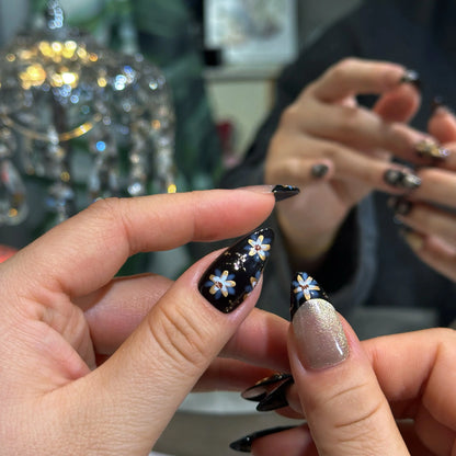 Elegant manicure with Raven Blossom black floral press on nails worn on hand.