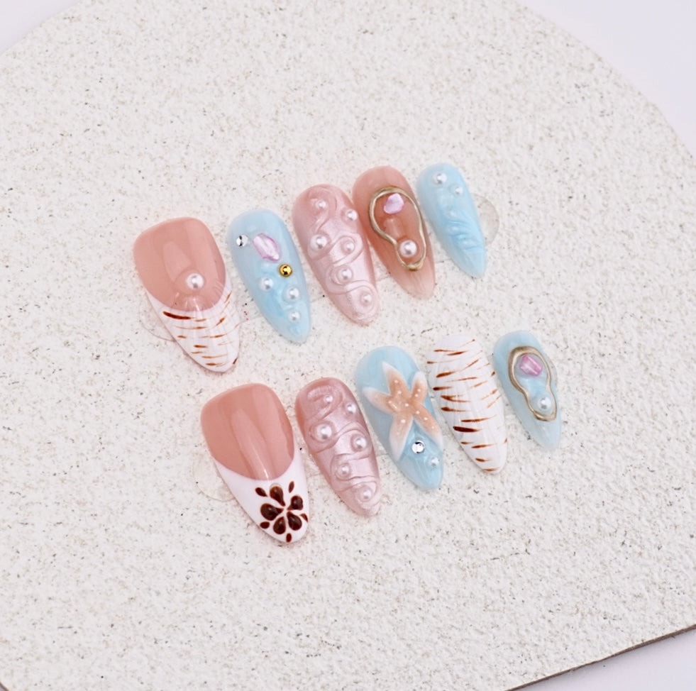 Handmade press-on nails featuring 3D starfish charm, white pearls, blue swirls, and brown french tip design.


