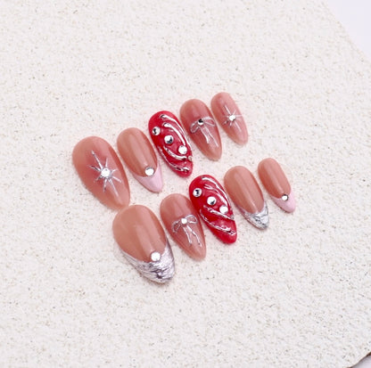 Almond press-on nails featuring 3D silver bows, stars, red chrome liquid swirls, and french tips.

