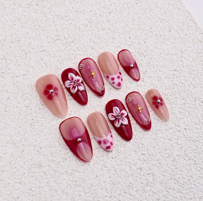 Almond press-on nails featuring cherry red aura blush, white 3D flower, gold star charm, and polka dot french tips.

