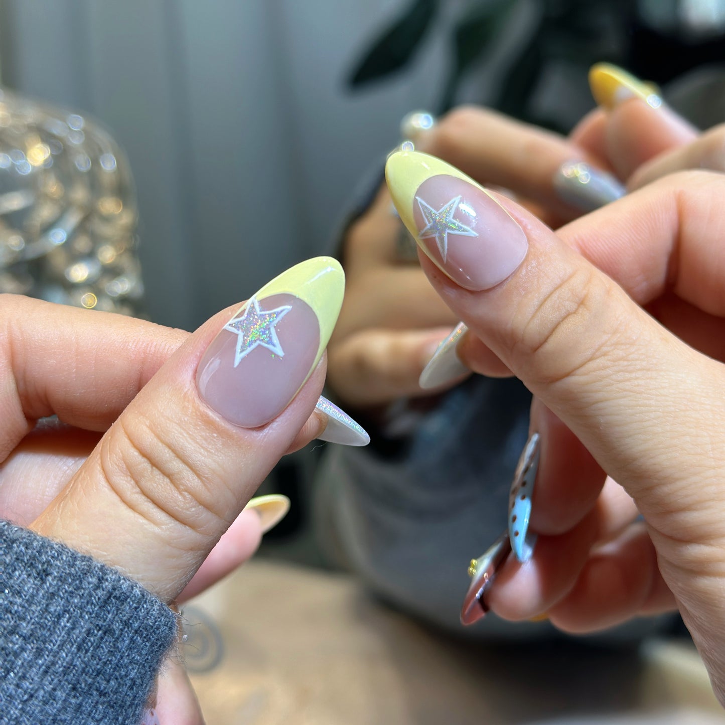 Close-up of Starry Dots nails showing holographic white star accents with yellow tips and chrome finish
