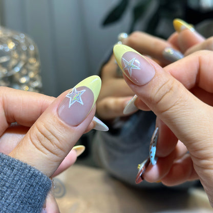 Close-up of Starry Dots nails showing holographic white star accents with yellow tips and chrome finish
