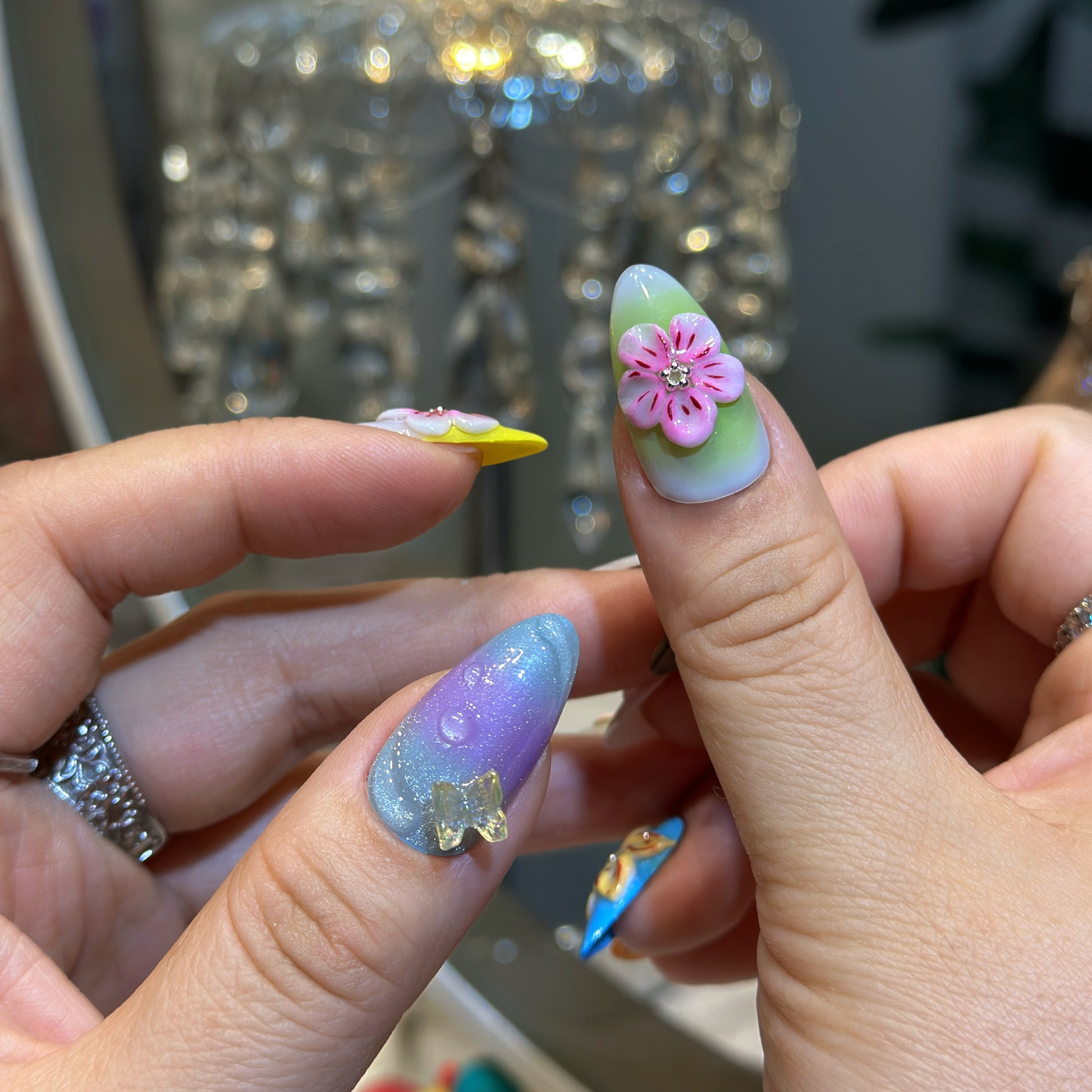 Close-up of Rainbow Garden press-on nails showing 3D dimensional flowers with crystal centers and butterfly patterns
