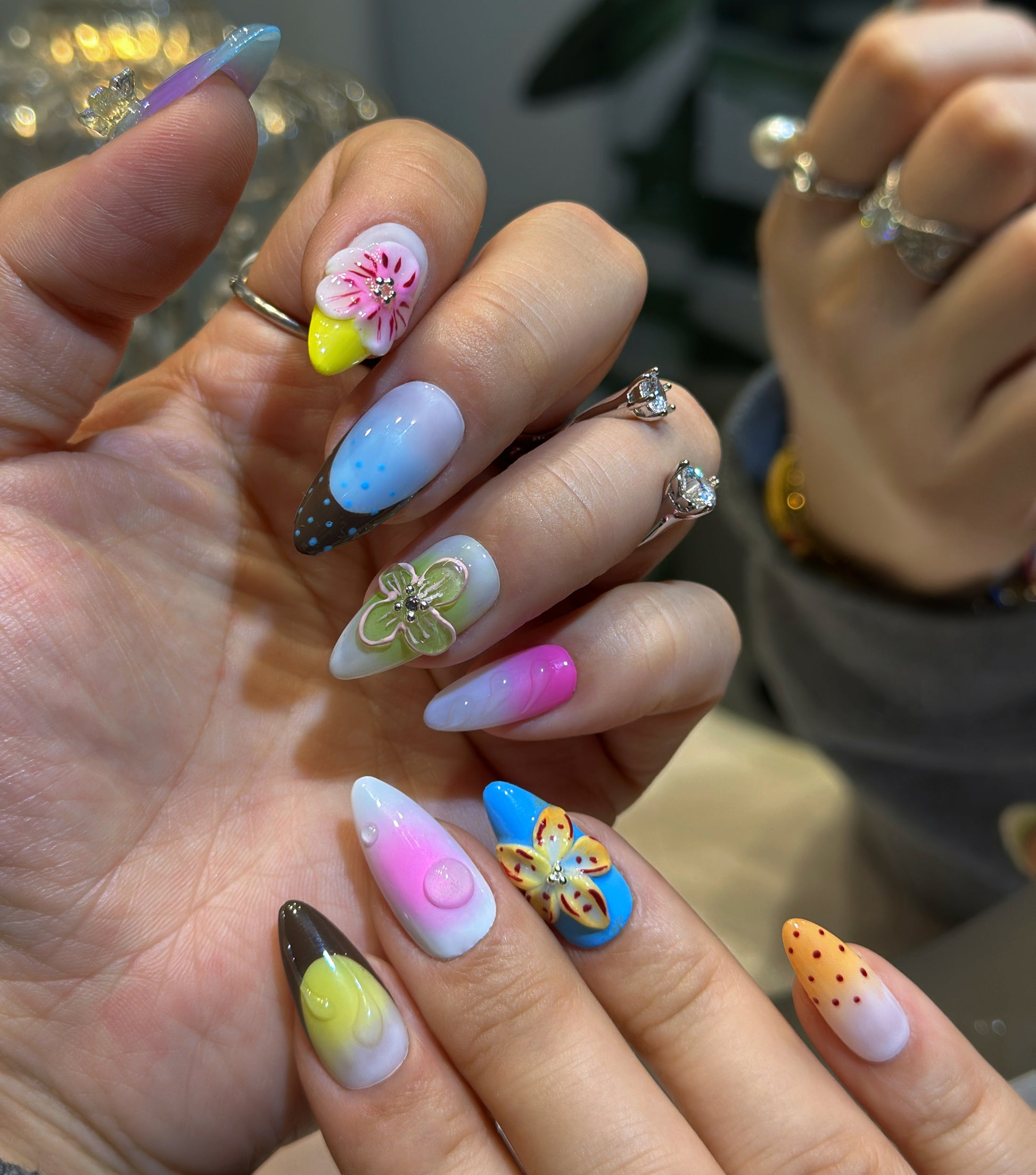 Both hands wearing Rainbow Garden nails with colorful polka dots, floral accents and sparkling rhinestone embellishments
