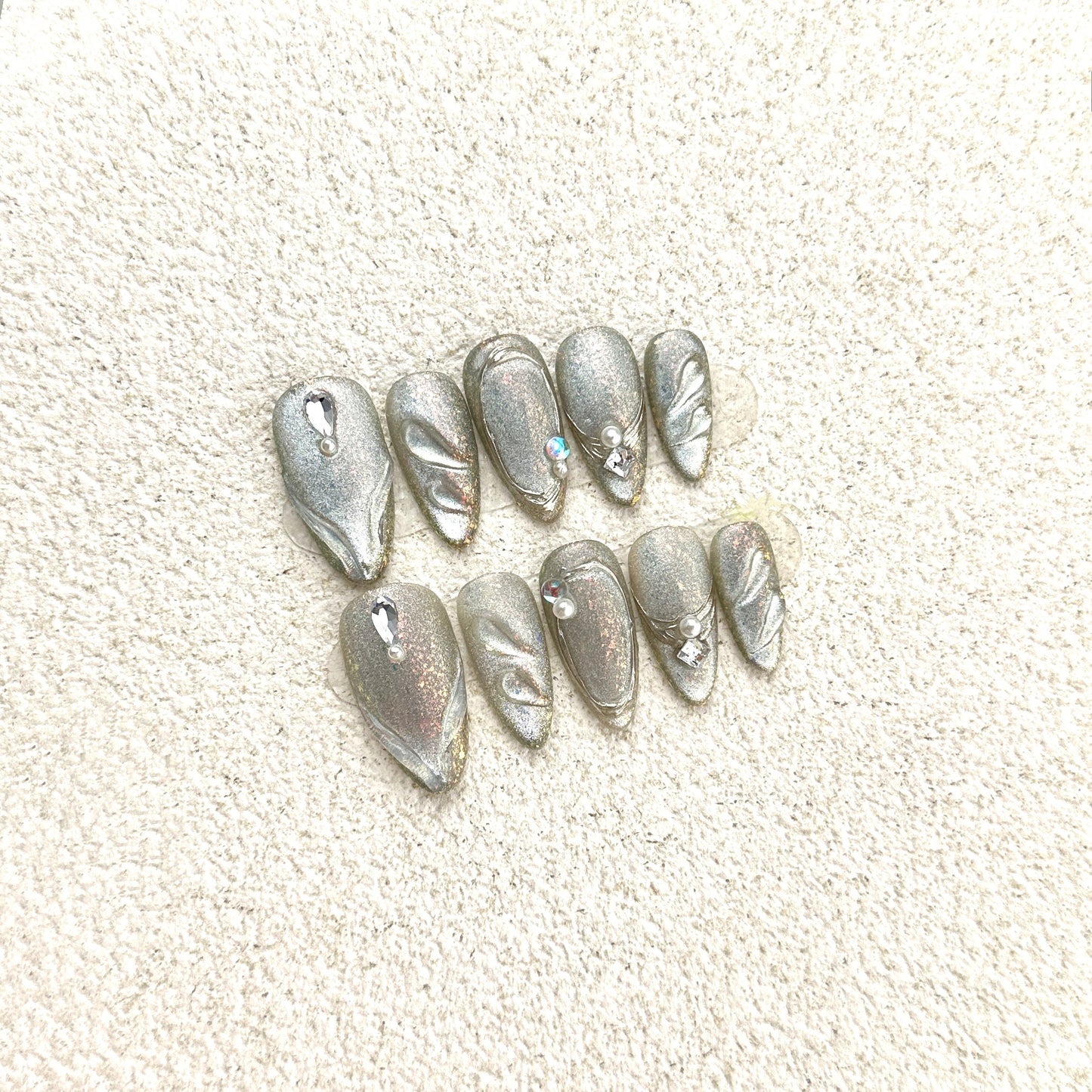 Silver Feather press-on nails flat lay with full-coverage silver glitter, leaf and feather patterns, crystal and pearl accents
