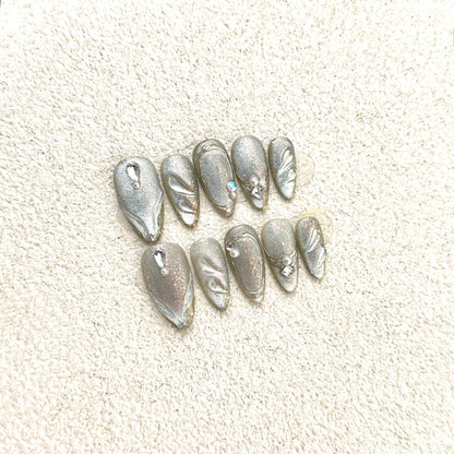 Silver Feather press-on nails flat lay with full-coverage silver glitter, leaf and feather patterns, crystal and pearl accents
