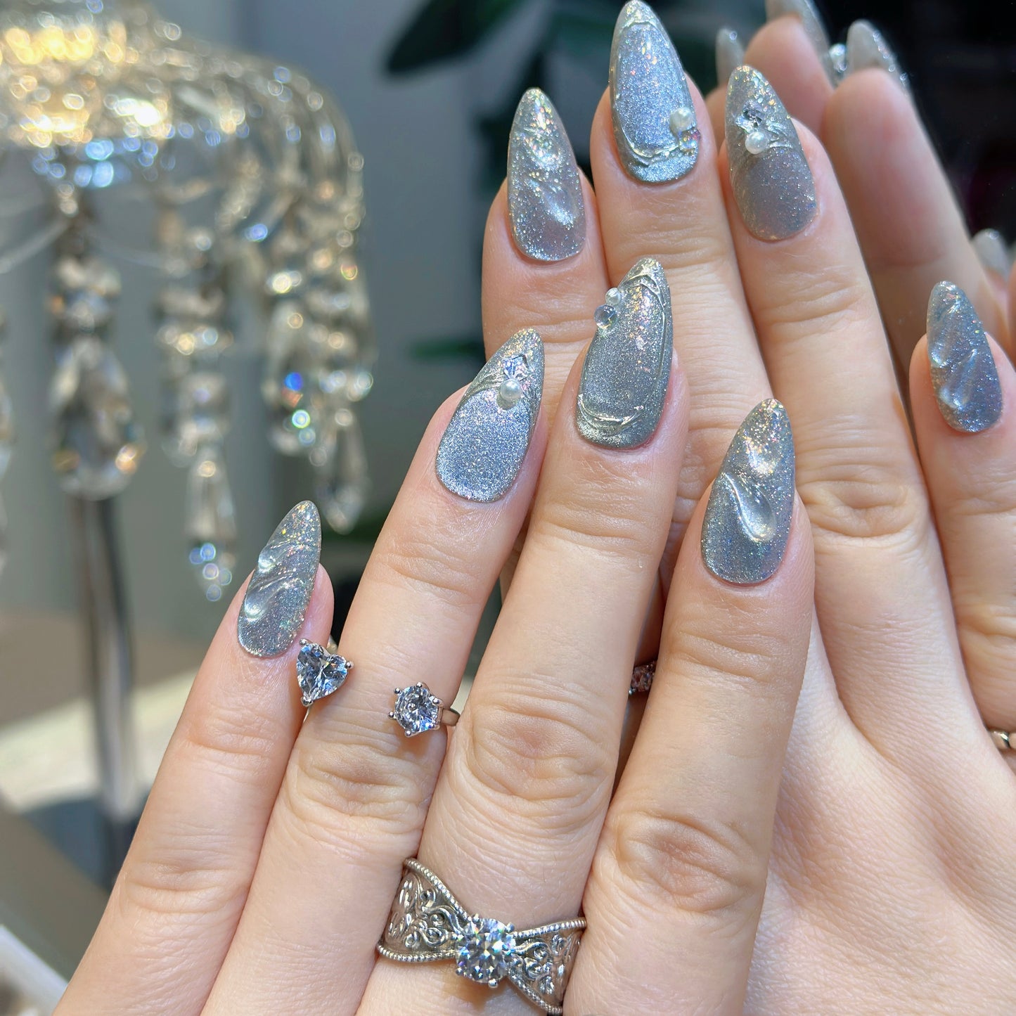 Hand modeling Silver Feather nails displaying shimmering silver-gray glitter base with delicate feather textures
