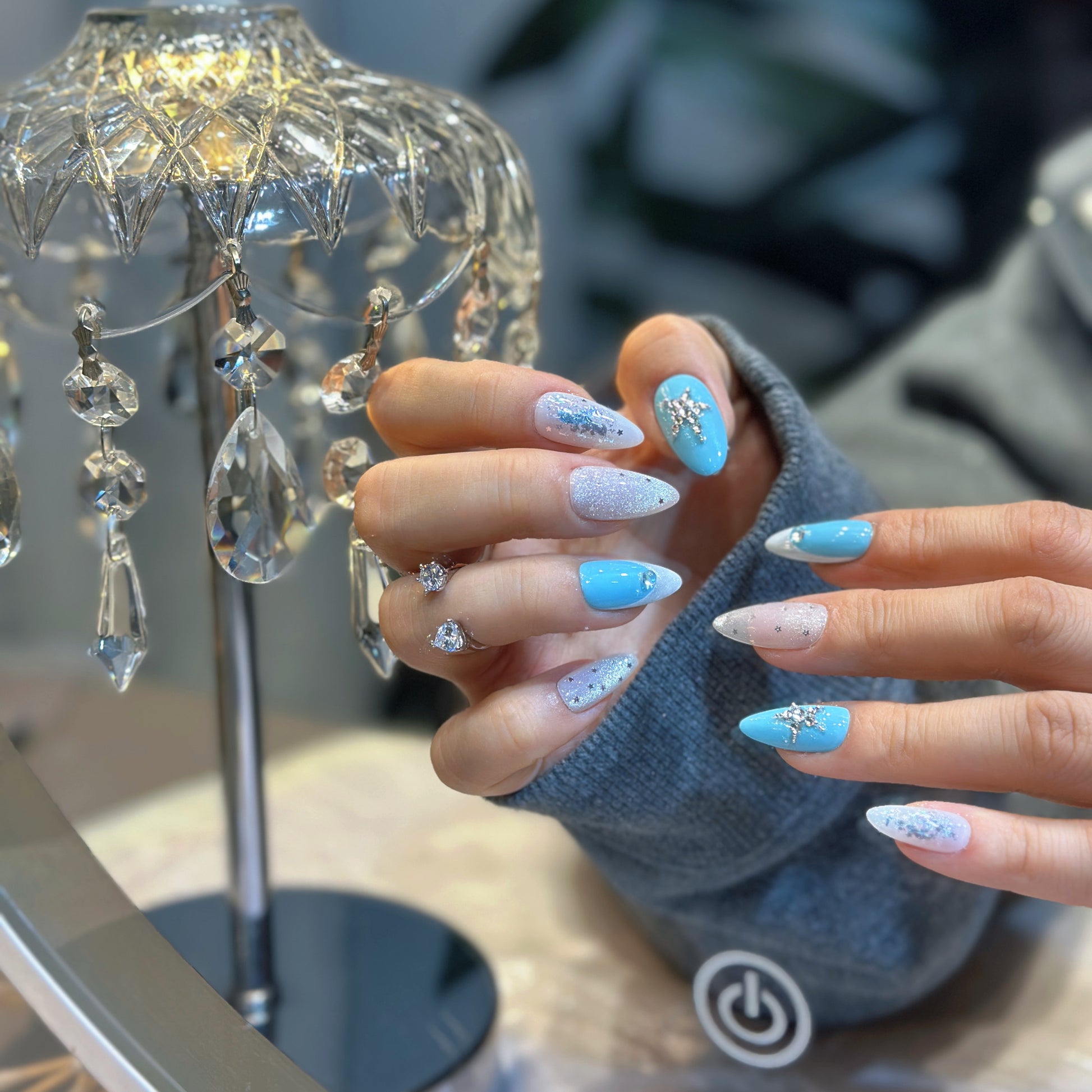 Close-up of Celestial Cross press-on nails showing shimmering silver glitter with delicate star accents and glossy finish
