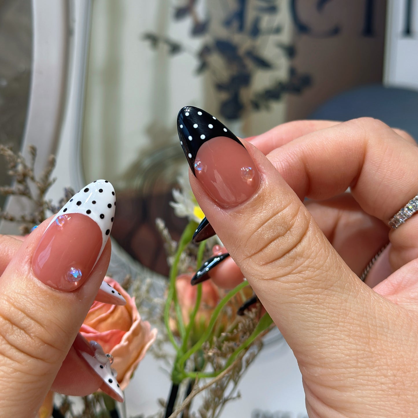 Hand modeling Polka Dot Bloom nails showing black French tips with white polka dots and white tips with black dots
