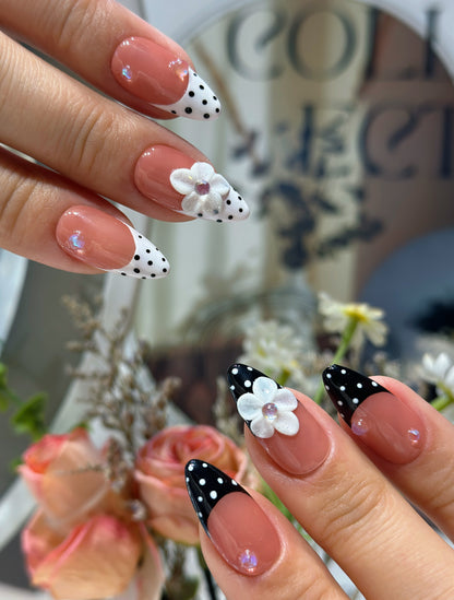 Both hands wearing Polka Dot Bloom nails with retro black and white polka dot design and dimensional floral embellishments
