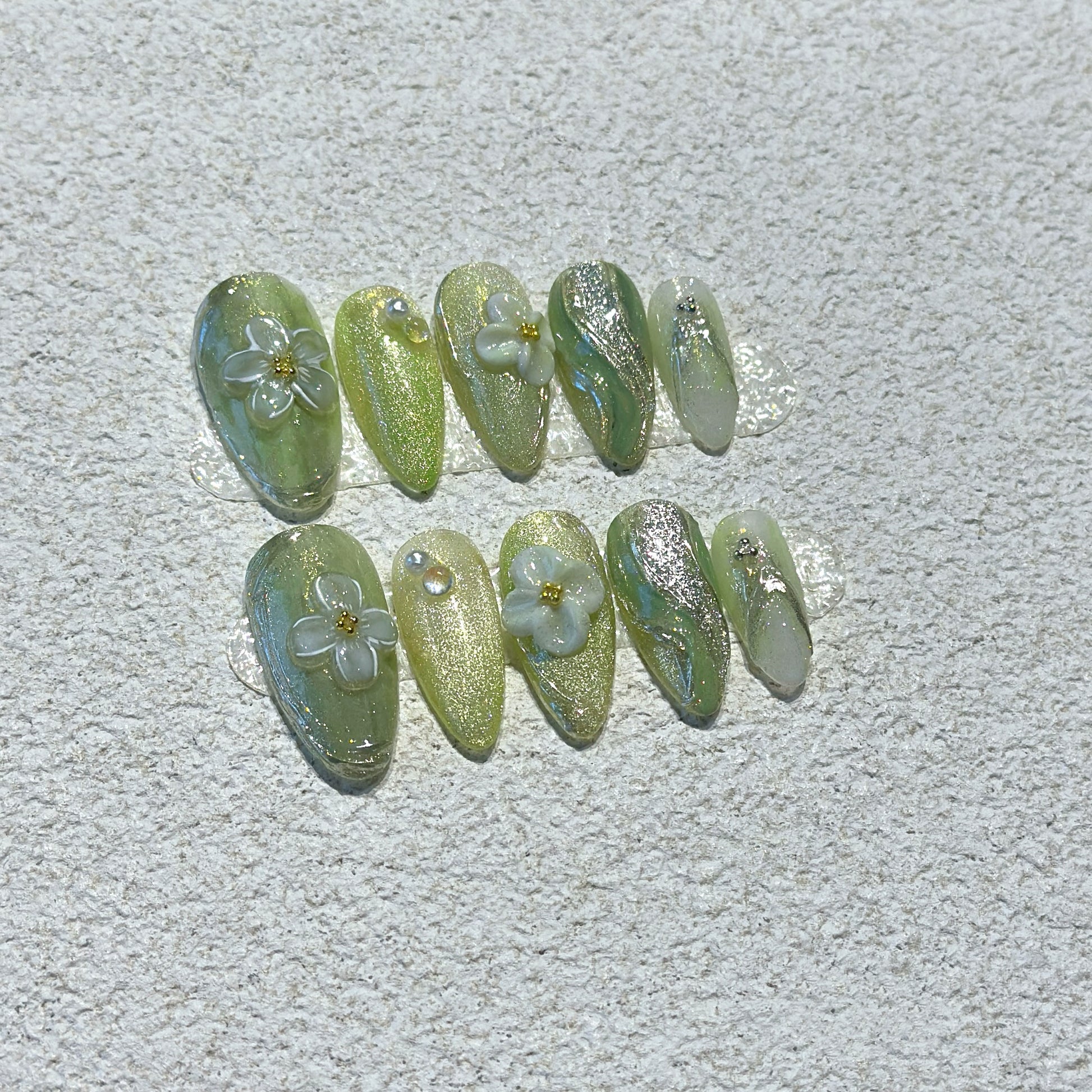 Matcha Daisy Garden press-on nails showing sage green base with silver glitter shimmer and 3D white daisy flowers with gold centers

