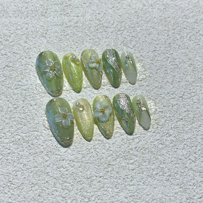 Matcha Daisy Garden press-on nails showing sage green base with silver glitter shimmer and 3D white daisy flowers with gold centers
