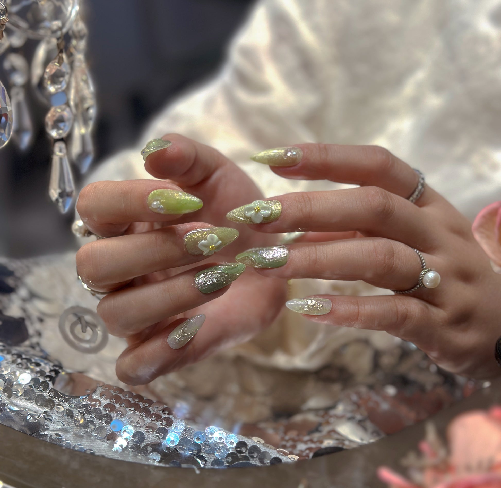 Hand modeling Matcha Daisy Garden nails beside fresh daisies showing green marble swirl texture and dimensional white floral accents
