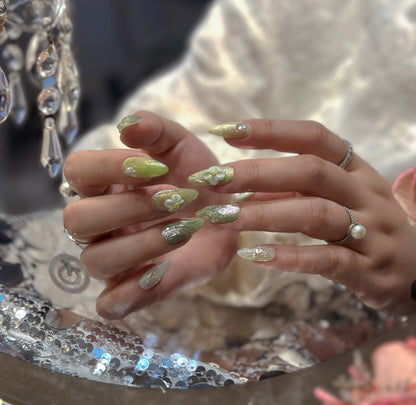 Hand modeling Matcha Daisy Garden nails beside fresh daisies showing green marble swirl texture and dimensional white floral accents
