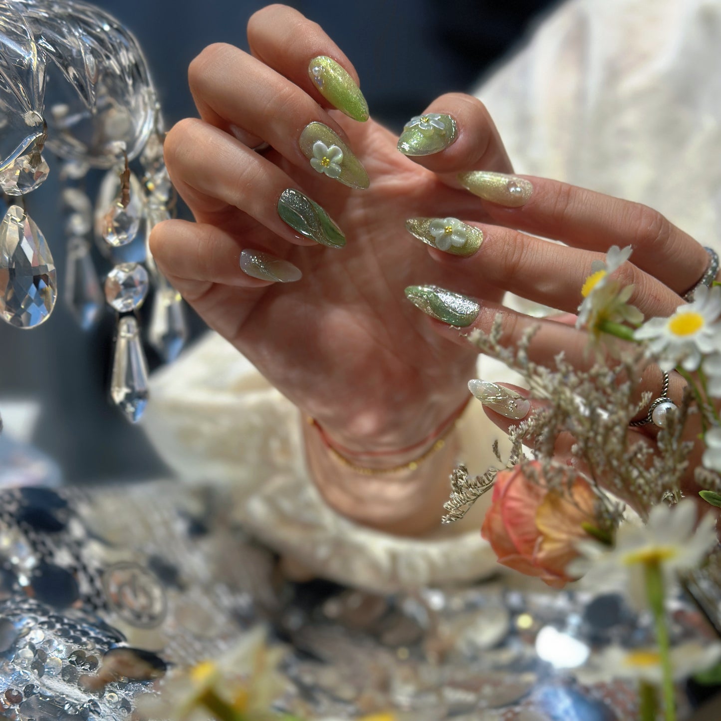 Both hands holding flowers wearing Matcha Daisy Garden nails with 3D white daisies and iridescent aurora crystal rhinestones

