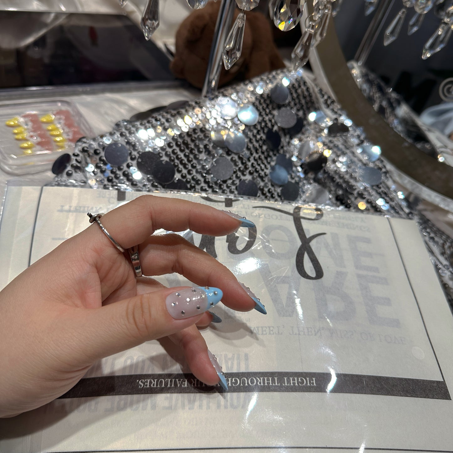 Single hand wearing Blue French Crystal Rain press-on nails with crystal chandelier showing almond shape and blue French tip detail
