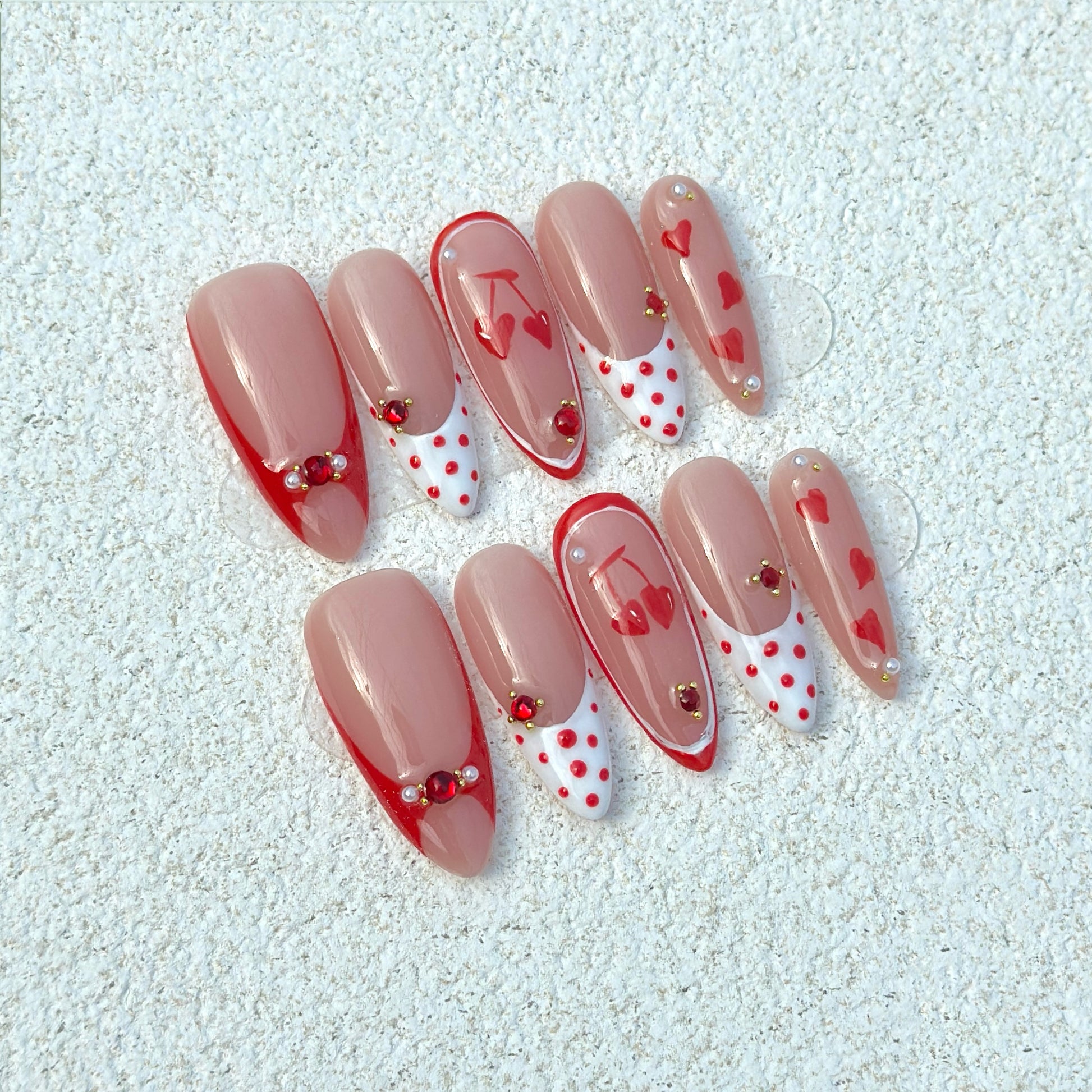 Cherry Love Polka press-on nails flat lay with nude base, red French tip outlines, white polka dot tips, cherry illustrations and heart motifs
